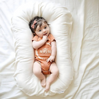 Bébé souriant allongé sur un coussin blanc, portant un body orange avec un nœud dans les cheveux. Photographie de bébé, mignon, confort.