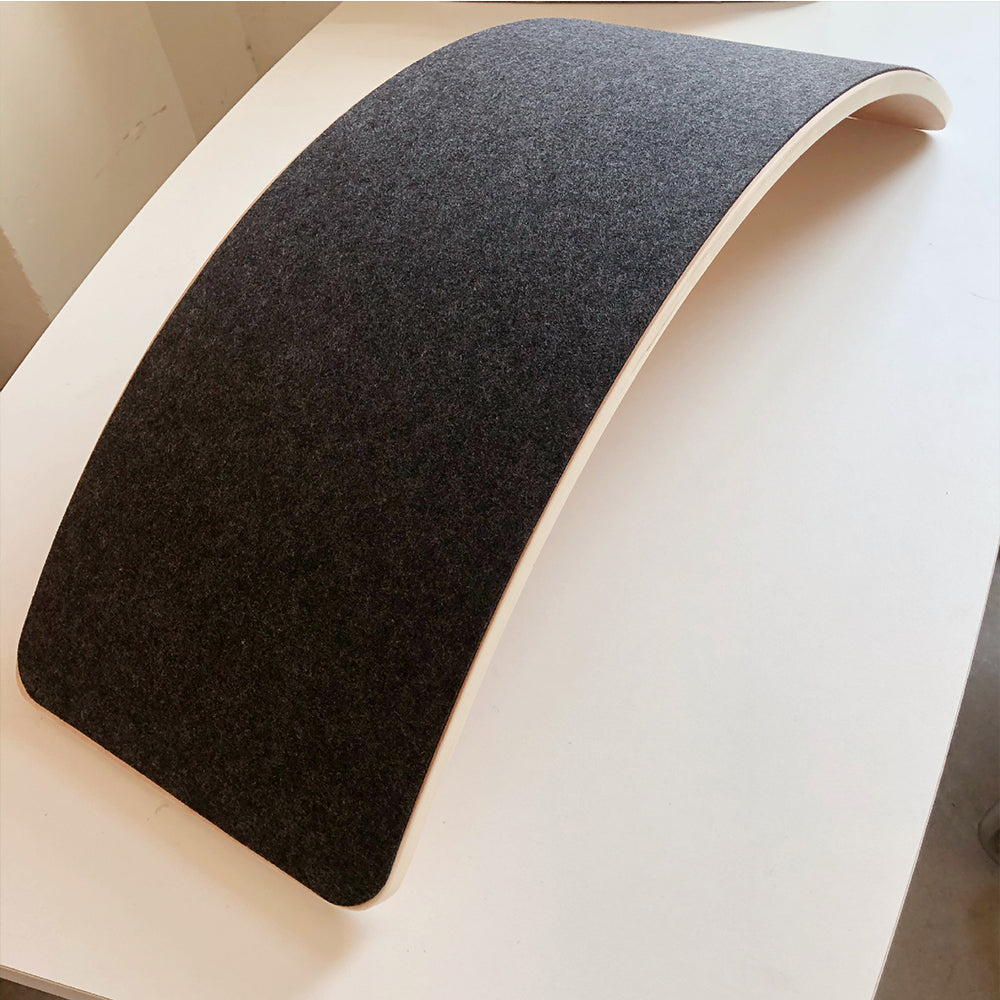 Arc de yoga en bois avec surface en feutre gris, posé sur une table blanche. Accessoire de fitness pour étirements et renforcement musculaire.