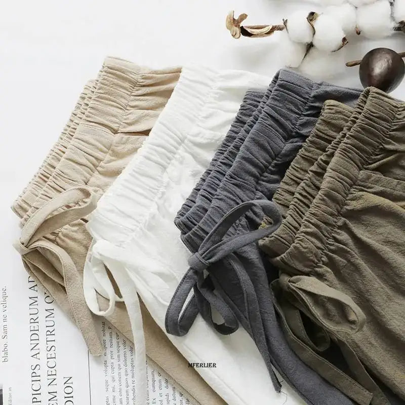 Shorts en lin pour femmes, couleurs beige, blanc, gris et kaki, posés sur un magazine avec des branches de coton, mode estivale décontractée.