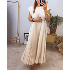 Robe longue plissée blanche élégante portée par une femme, accessoires dorés, miroir, décoration intérieure moderne, ambiance chic et minimaliste.