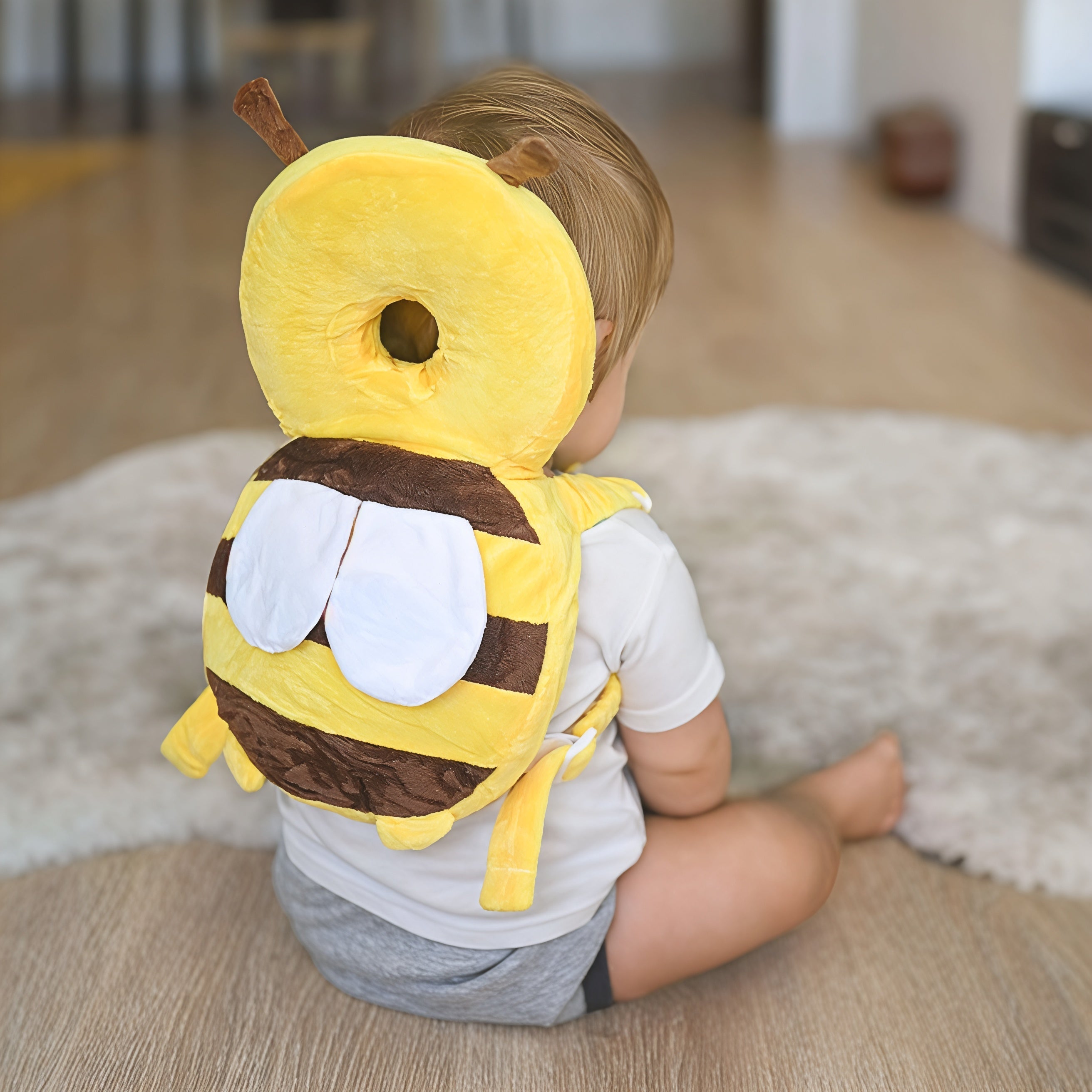 Enfant assis portant un coussin de protection jaune en forme d'abeille, sur un tapis beige. Sécurité bébé, protection tête, design mignon.