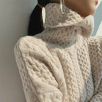 Femme portant un pull en laine torsadée beige à col roulé, style automne-hiver, mode féminine élégante, gros plan sur le tissu texturé.