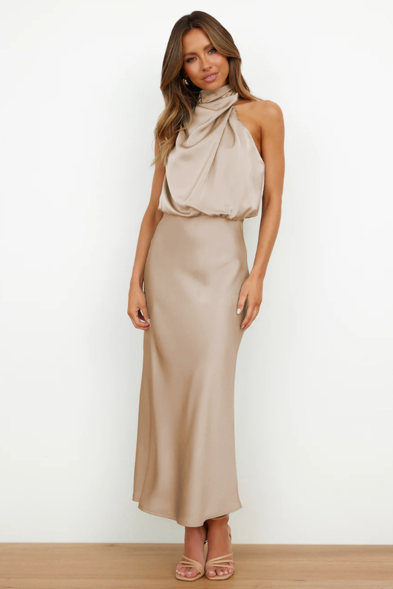 Robe longue beige élégante en satin, col drapé, sans manches, portée par une femme. Mode féminine chic, tenue de soirée tendance.