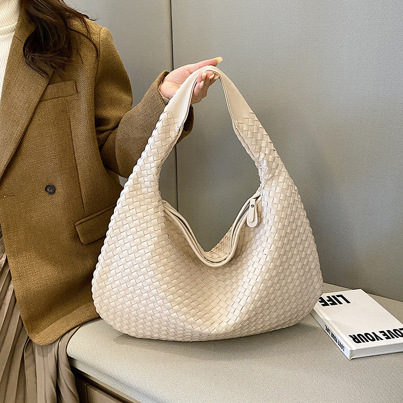 Sac à main tissé beige élégant, porté par une femme en manteau marron, posé sur un banc avec un livre. Accessoire mode tendance et chic.