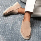 Mocassins en daim beige pour homme sur tapis gris, portés avec un pantalon blanc. Chaussures élégantes, confortables, style décontracté chic.