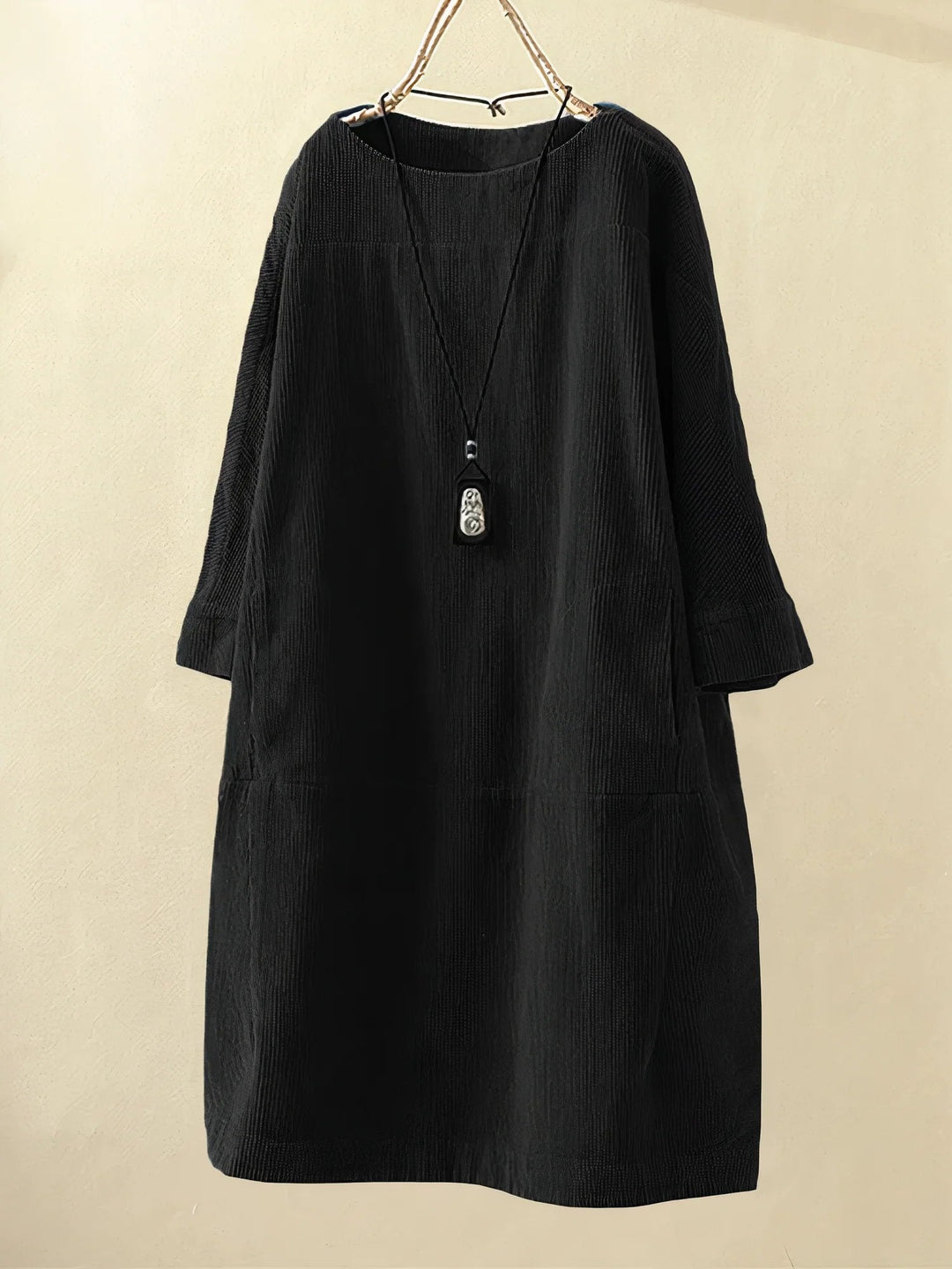 Robe noire en velours côtelé, manches longues, coupe ample, avec collier pendentif. Mode féminine élégante, style décontracté automne-hiver.