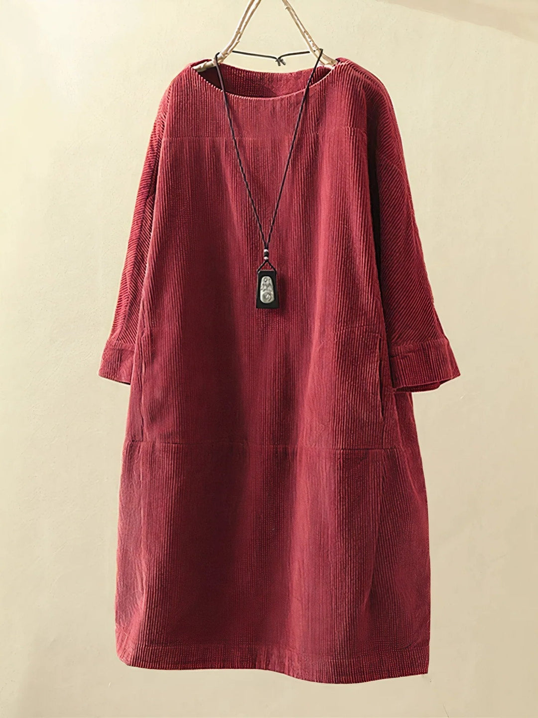 Robe en velours côtelé rouge bordeaux, manches longues, col rond, avec pendentif noir suspendu. Mode automne-hiver, style décontracté élégant.