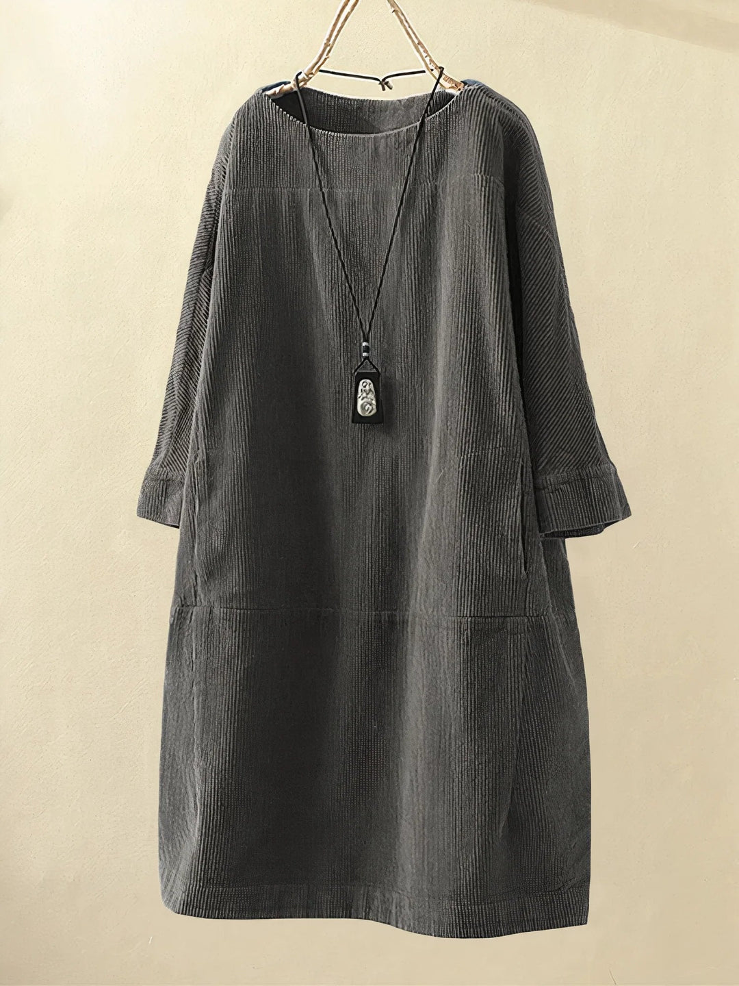 Robe ample en velours côtelé gris avec col rond, manches longues et pendentif noir suspendu. Mode automne-hiver, style décontracté et élégant.