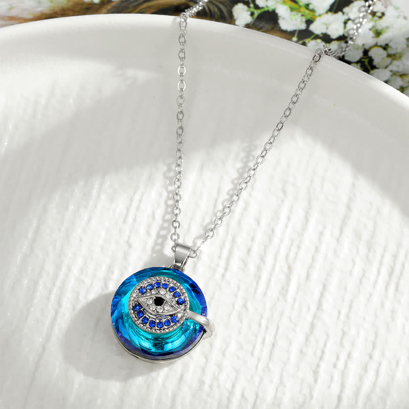 Collier pendentif en argent avec cristal bleu et motif œil protecteur, posé sur une assiette blanche. Bijoux élégants, tendance mode.