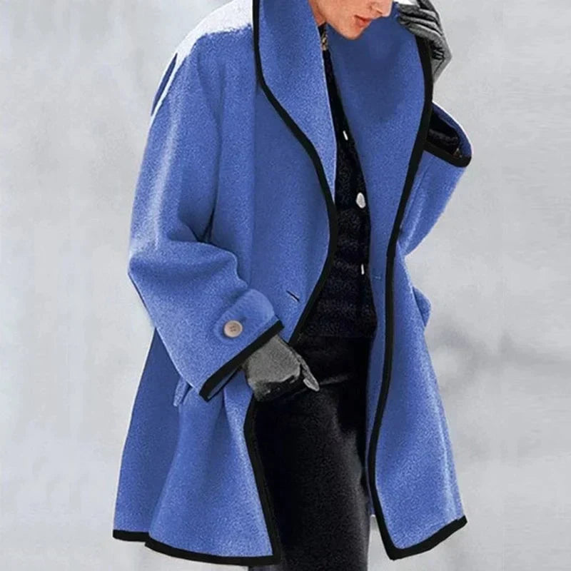 Manteau bleu femme élégant avec bordure noire, manches longues, boutons décoratifs, porté avec des gants gris. Mode hiver chic et tendance.