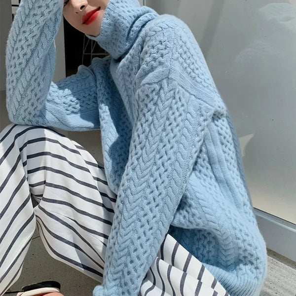 Femme portant un pull en laine bleu ciel torsadé, assise avec un pantalon à rayures noires et blanches. Mode automne-hiver, style décontracté.