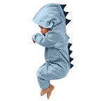 Bébé en combinaison dinosaure bleue avec capuche et crêtes noires, dormant paisiblement. Pyjama mignon, vêtement bébé, déguisement dinosaure.