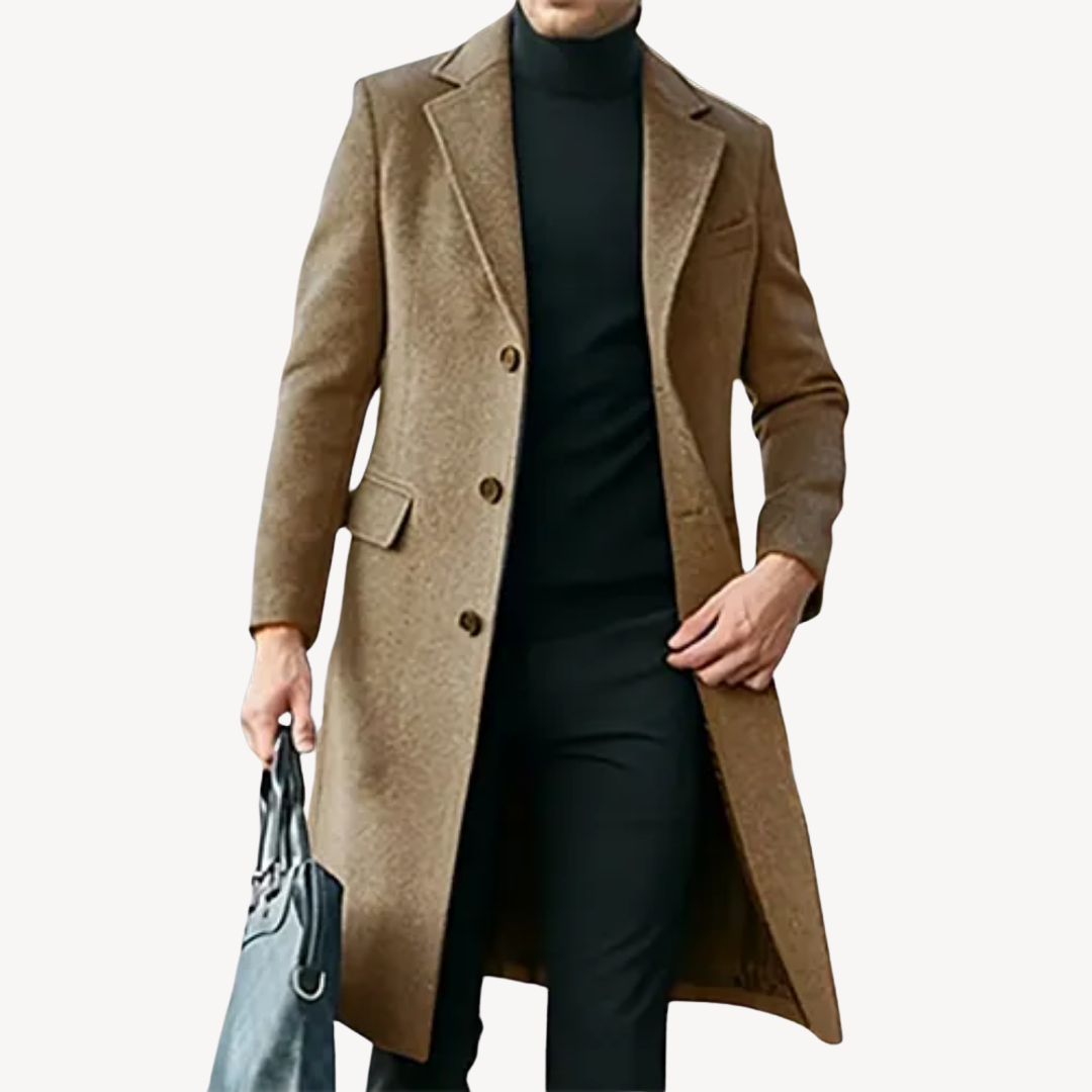 Manteau long homme marron élégant, porté avec un pull noir et un pantalon noir, tenant un sac gris. Mode masculine chic et moderne.