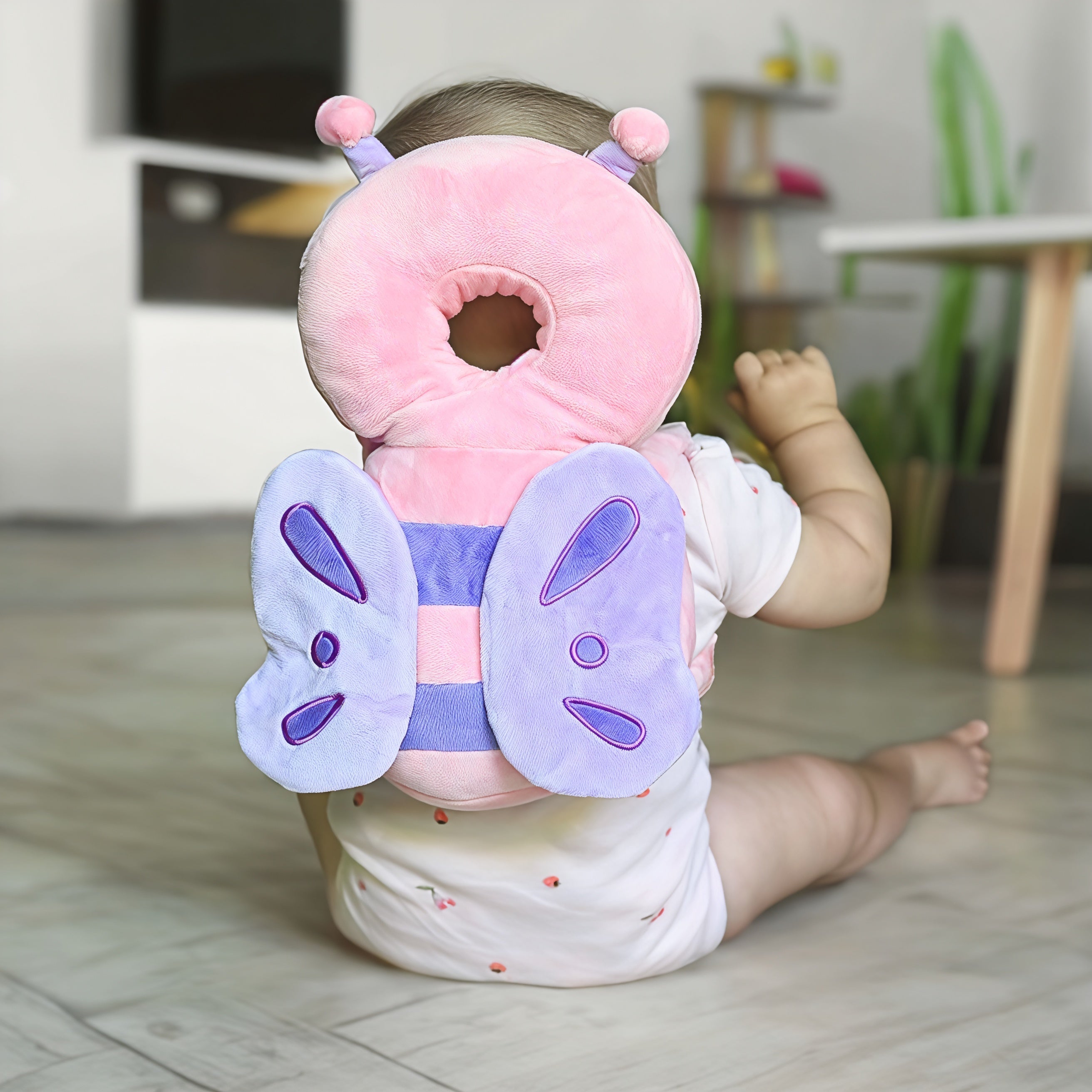 Bébé assis portant un coussin de protection rose en forme de papillon, idéal pour la sécurité des tout-petits. Accessoire bébé, protection tête.