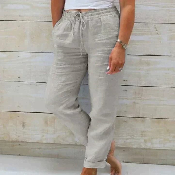 Pantalon en lin beige pour femme, style décontracté avec cordon de serrage, poches latérales, fond en bois clair, mode estivale confortable.