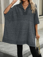 Femme portant un poncho gris à col zippé, accessoirisé d'un sac à chaîne dorée. Mode automne, tenue décontractée chic, rue pavée en arrière-plan.