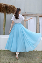 Femme en jupe longue bleue virevoltante, t-shirt blanc, posant en extérieur. Mode féminine, élégance estivale, style décontracté.