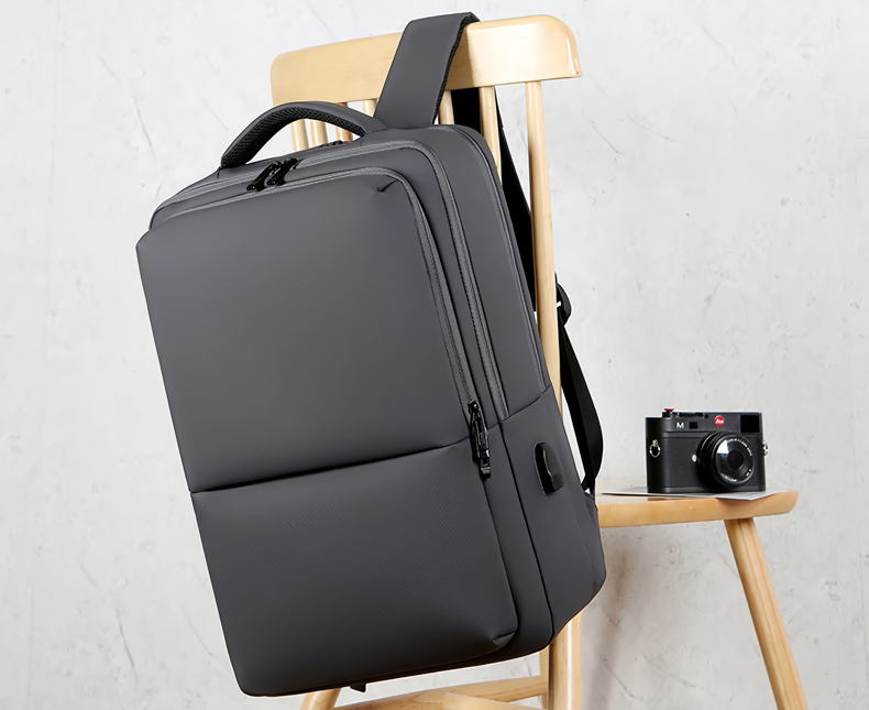 Sac à dos noir moderne sur chaise en bois, appareil photo vintage à côté. Design minimaliste, idéal pour voyage, travail, étudiants.