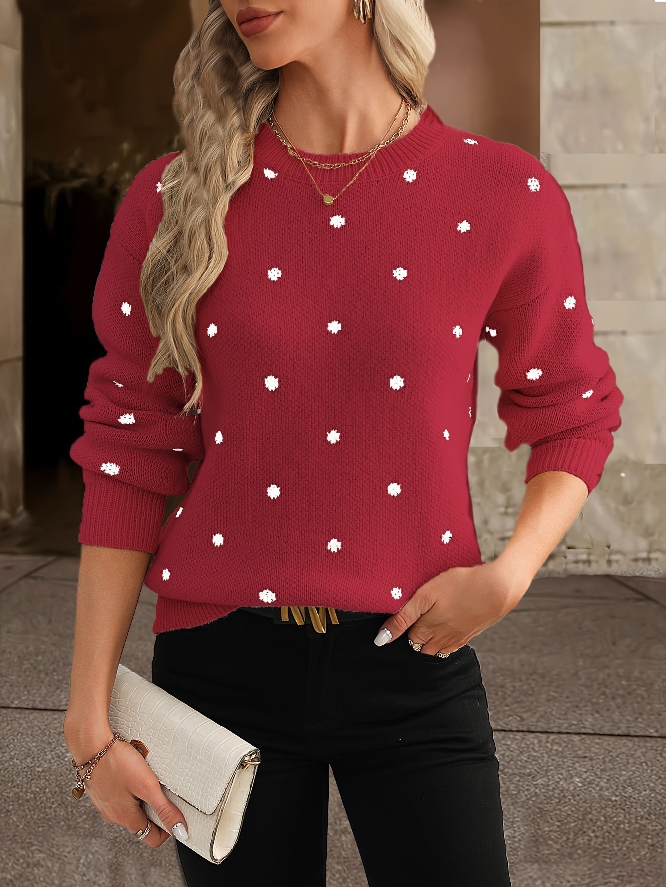 Femme portant un pull rouge à pois blancs, tenant une pochette blanche. Mode automne, style décontracté chic, cheveux blonds ondulés.