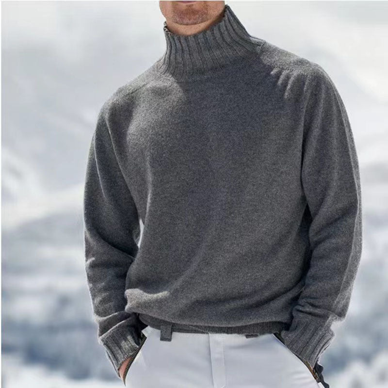 Homme portant un pull en cachemire gris à col roulé, fond enneigé. Mode hiver élégante, vêtements chauds, style décontracté chic.