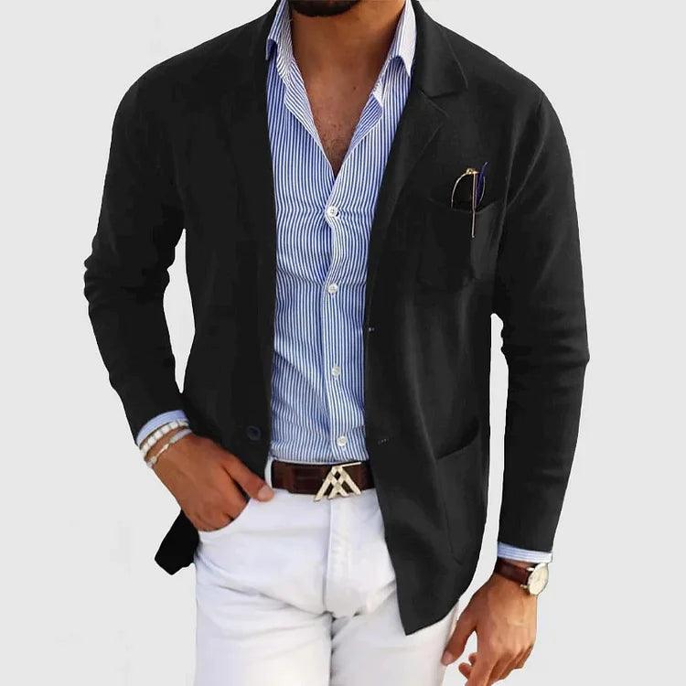 Homme en blazer noir élégant, chemise rayée bleue, pantalon blanc, montre-bracelet, bracelet perles, style mode masculine chic et moderne.