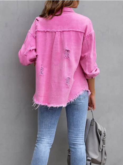 Femme portant une chemise en jean rose déchirée, manches retroussées, associée à un jean bleu clair, tenant un sac à main gris. Mode décontractée tendance.