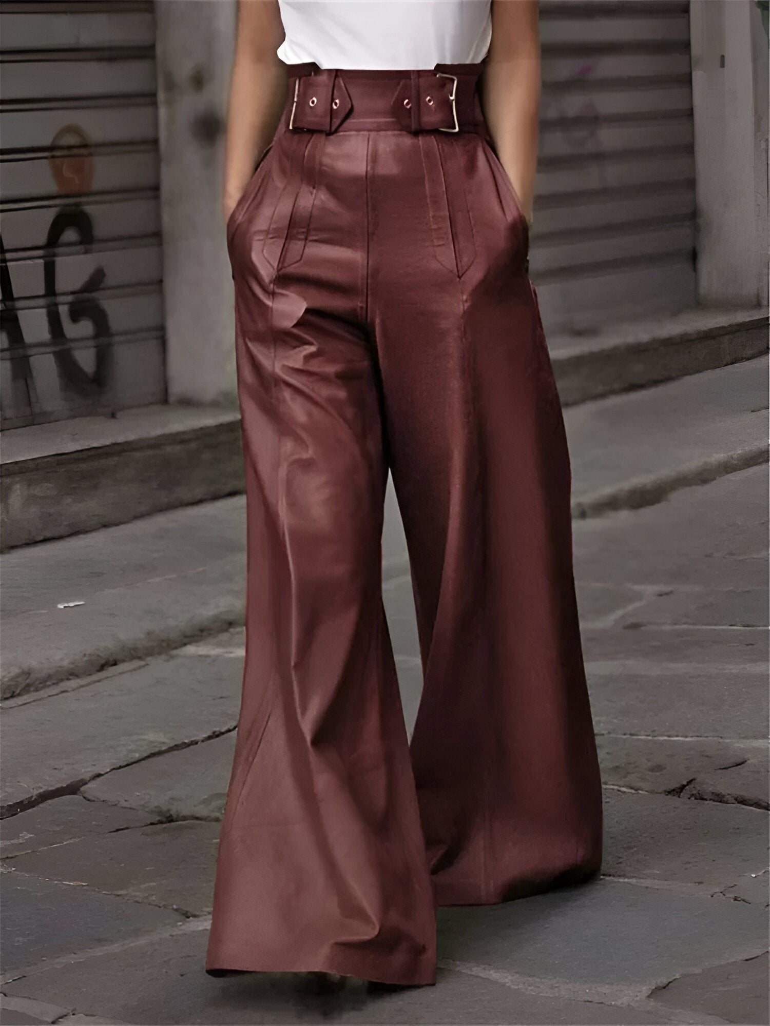Femme portant un pantalon large en cuir marron, taille haute avec ceinture, marchant en ville. Mode urbaine élégante, tendance automne.