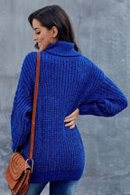Femme portant un pull bleu en tricot épais, col roulé, avec un sac en cuir marron. Mode automne-hiver, style décontracté et élégant.