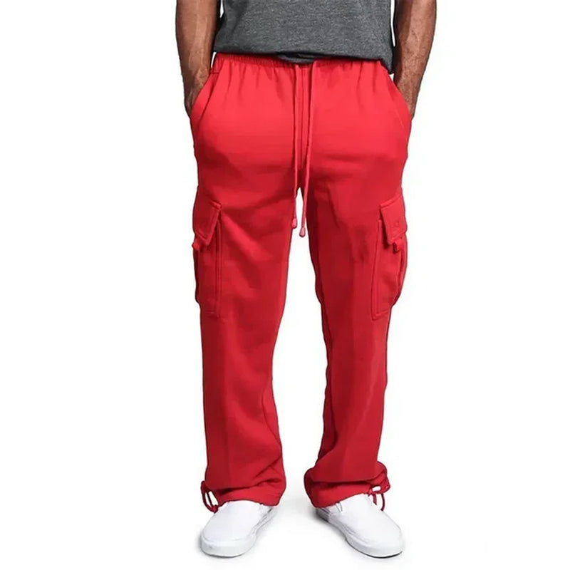 Pantalon cargo rouge pour homme, avec poches latérales, cordon de serrage, porté avec un t-shirt gris et des baskets blanches.