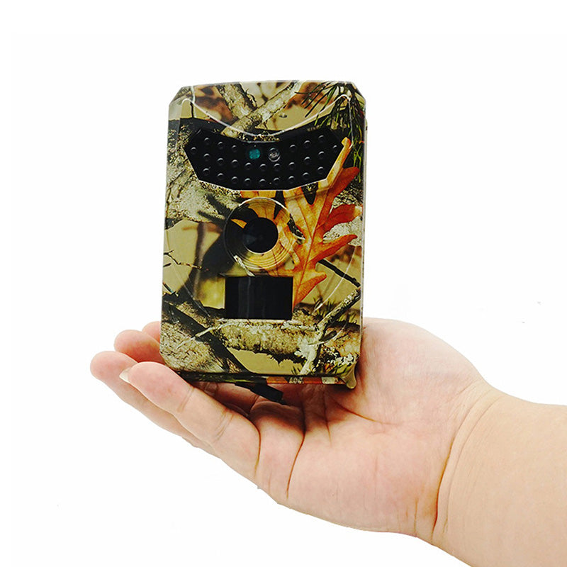 Appareil photo de chasse camouflage tenu dans une main, idéal pour la surveillance de la faune. Design compact, capteur infrarouge intégré.