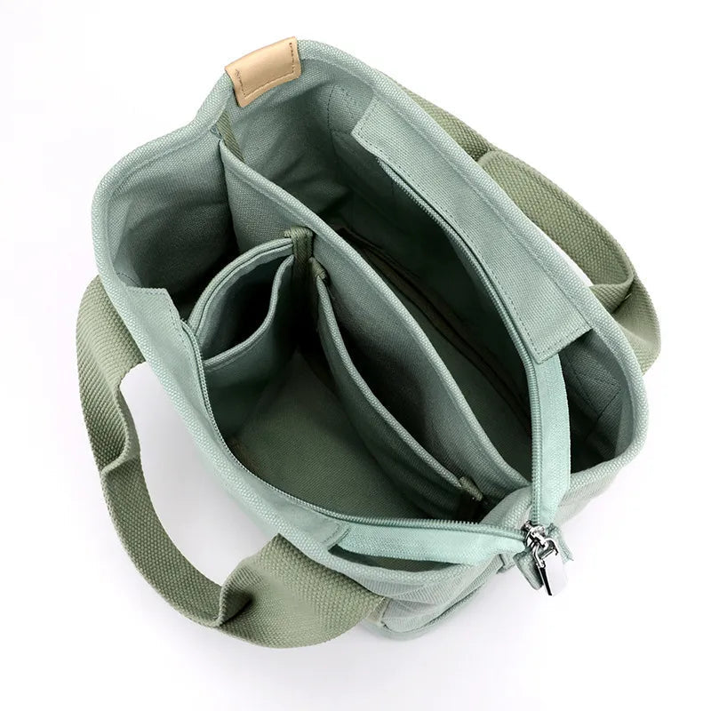 Sac à main vert menthe en toile avec plusieurs compartiments, fermeture éclair et poignées robustes. Accessoire mode pratique et tendance.