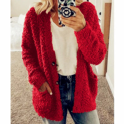 Femme portant un cardigan rouge en tricot texturé, tenant un smartphone avec coque design, vêtue d'un t-shirt blanc et d'un jean décontracté.