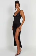 Femme portant une robe noire élégante avec bretelles fines et fente haute, posant sur fond blanc. Mode féminine, robe de soirée chic.