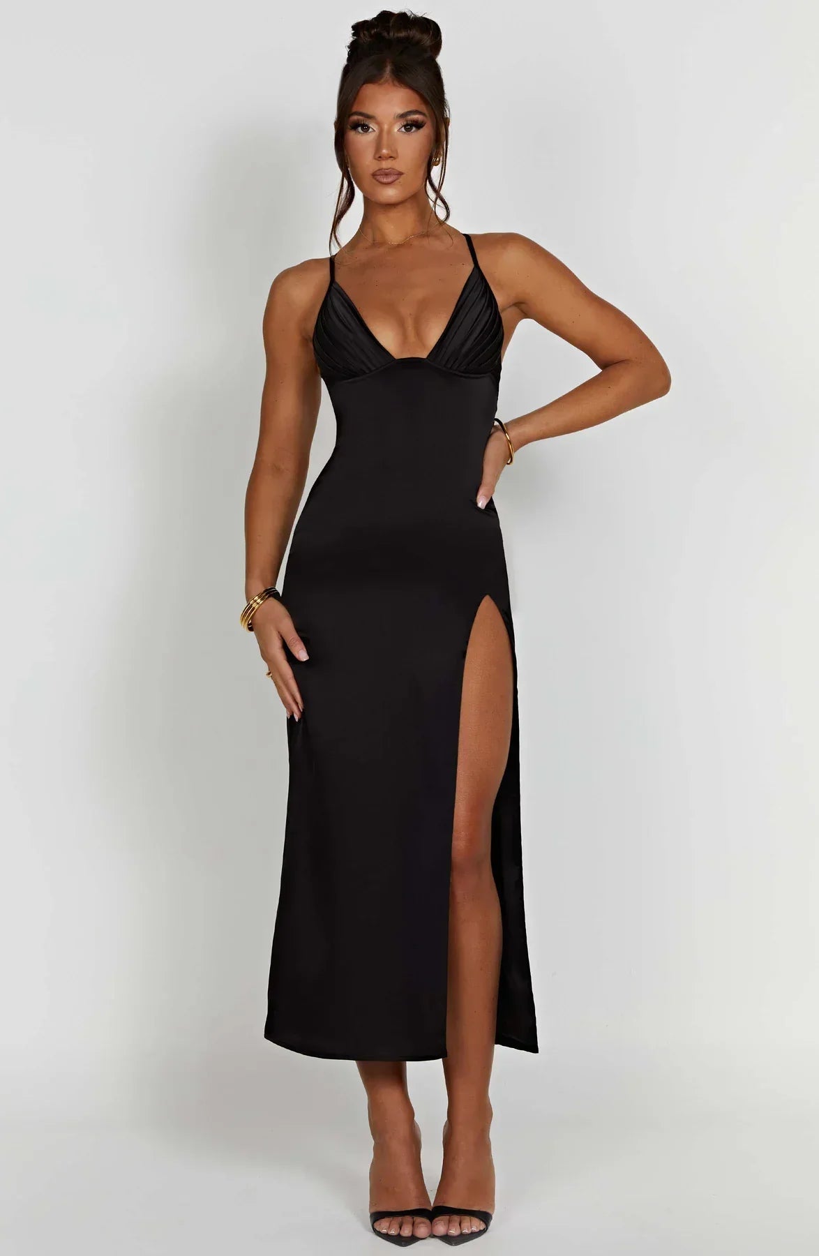 Robe longue noire élégante avec fente haute, bretelles fines et décolleté plongeant, portée par une femme. Mode soirée chic et tendance.