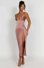 Robe longue satinée rose avec bretelles fines et fente haute, portée par une femme. Mode élégante, tenue de soirée chic, style glamour.