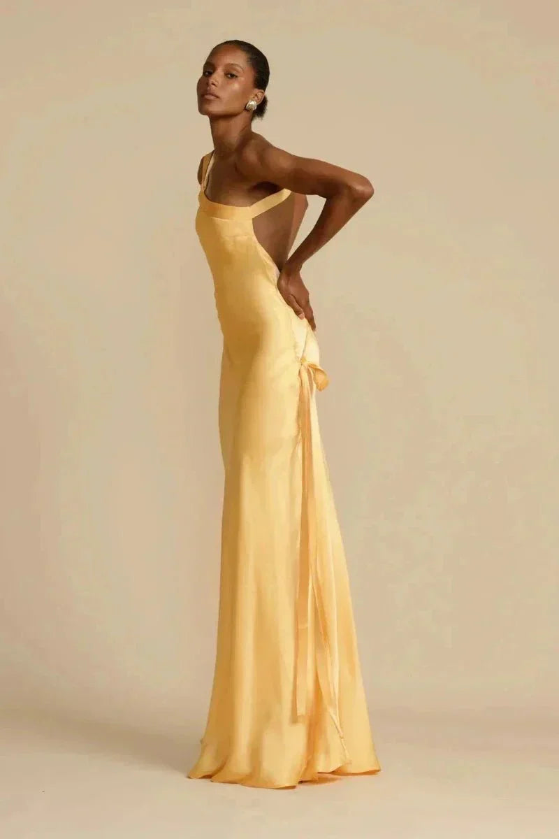 Robe longue satinée jaune, élégante et fluide, portée par une femme posant de profil. Mode féminine, tenue de soirée chic, style glamour.