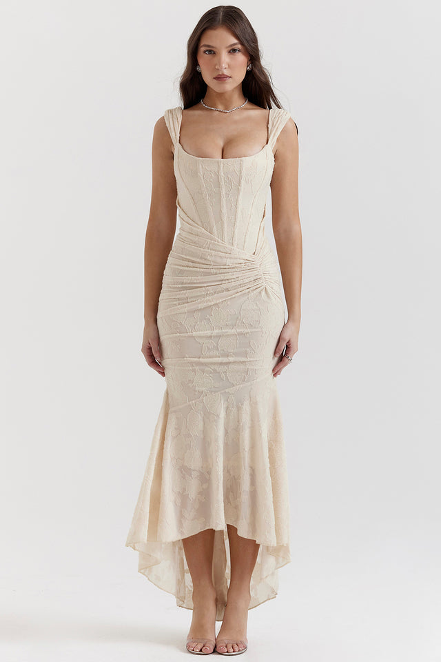 Robe longue beige élégante avec dentelle, décolleté carré et ourlet asymétrique, portée par une femme. Mode féminine chic et tendance.