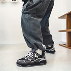 Pantalon ample en denim noir avec baskets noires et blanches, style streetwear moderne, sol blanc, intérieur minimaliste.