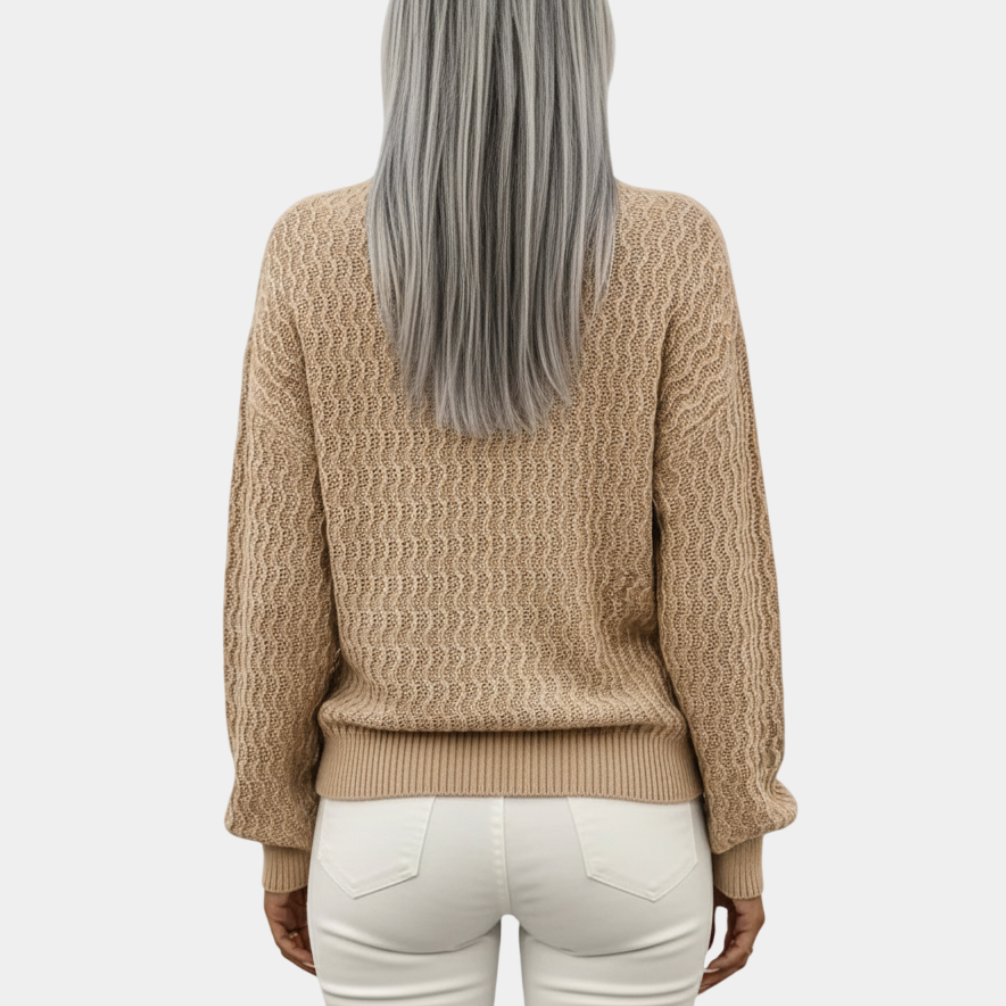 Femme aux cheveux gris portant un pull beige texturé et un pantalon blanc, vue de dos. Mode automne-hiver, style décontracté élégant.