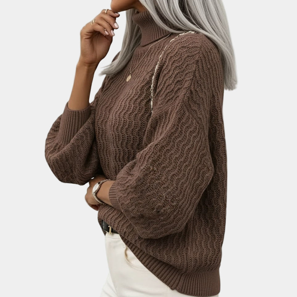 Femme portant un pull en maille marron à col roulé, manches longues, avec un collier doré, posant de profil. Mode automne-hiver élégante.