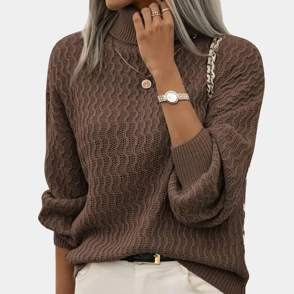 Femme portant un pull marron à col roulé texturé, montre argentée, collier doré, et pantalon blanc. Mode automne-hiver, style élégant et décontracté.