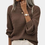 Femme portant un pull marron à col roulé texturé, montre argentée, collier doré, et pantalon blanc. Mode automne-hiver, style élégant et décontracté.
