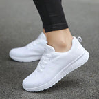 Chaussures de sport blanches pour femme sur fond de trottoir, design moderne et confortable, idéales pour la course et le fitness.