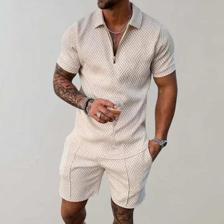 Homme en combishort beige à motifs géométriques, tenant une boisson. Mode masculine estivale, tenue décontractée élégante.