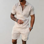 Homme en combishort beige à motifs géométriques, tenant une boisson. Mode masculine estivale, tenue décontractée élégante.