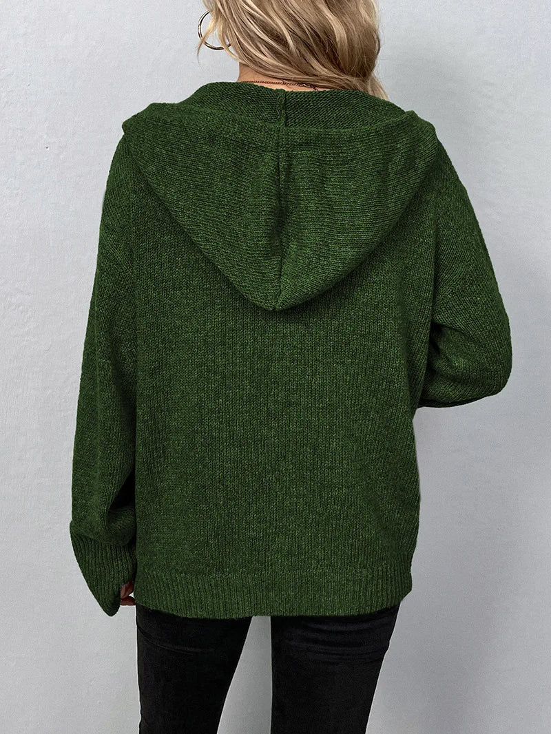 Femme portant un pull à capuche vert foncé en tricot, manches longues, dos visible. Mode automne-hiver, style décontracté et confortable.