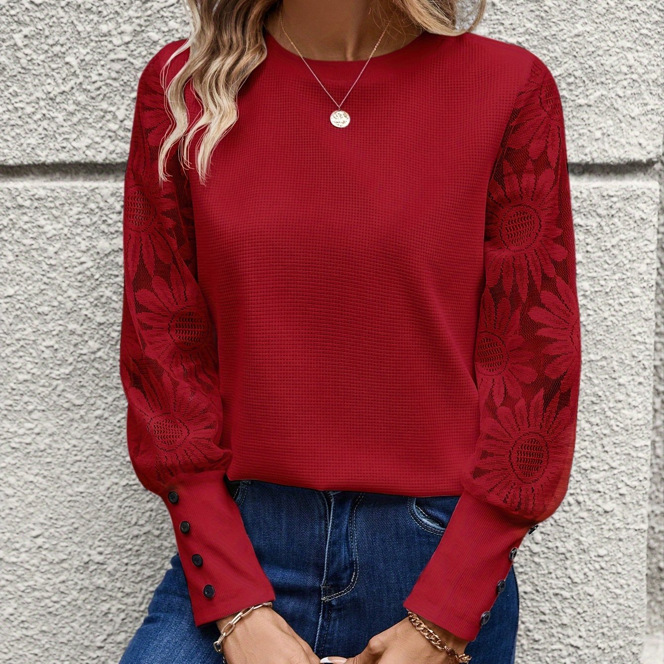 Blouse rouge à manches longues en dentelle florale, boutons décoratifs, portée avec un jean bleu. Mode féminine élégante et tendance.