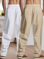 Deux pantalons de jogging pour homme, l'un blanc et l'autre beige, en tissu léger, présentés de dos dans un intérieur moderne et lumineux.