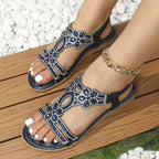 Sandales ornées de strass bleus et argentés sur pieds féminins, posées sur une terrasse en bois, avec bracelet chaîne doré. Mode estivale élégante.