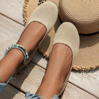 Ballerines beiges en toile sur pieds féminins, posées sur un sol en bois avec un chapeau de paille et un bracelet turquoise. Mode estivale décontractée.
